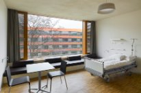 Patientenzimmer mit Spitalbett, Tisch und Stühle und Ausblick auf den Innenhof